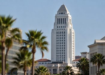 Los Angeles City Hall in neutral daylight, its tower sharp above softly blurred palm trees, illustrating the Los Angeles mayoral race.