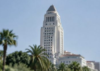 Los Angeles City Hall in neutral daylight, its tower sharp above softly blurred palm trees, illustrating the Los Angeles mayoral runoff.