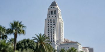 Los Angeles City Hall in neutral daylight, its tower sharp above softly blurred palm trees, illustrating the Los Angeles mayoral runoff.