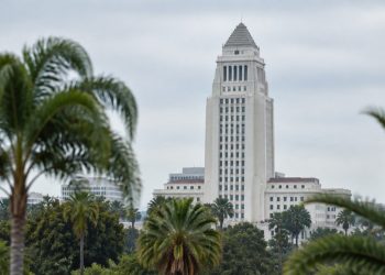 Los Angeles City Hall tower in neutral daylight above softly blurred palm trees, illustrating the Los Angeles mayoral runoff.