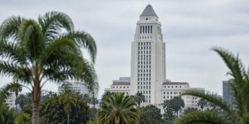 Los Angeles City Hall tower in neutral daylight above softly blurred palm trees, illustrating the Los Angeles mayoral runoff.