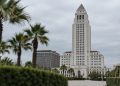 Los Angeles City Hall tower in neutral daylight, sharp above softly blurred palm trees, illustrating the debate over 2028 Olympics finances.