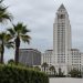 Los Angeles City Hall tower in neutral daylight, sharp above softly blurred palm trees, illustrating the debate over 2028 Olympics finances.
