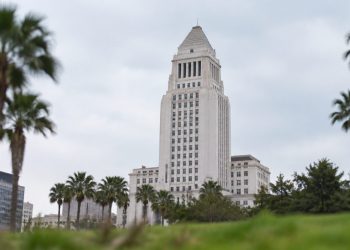 Los Angeles City Hall tower in neutral daylight, sharp above softly blurred palm trees in the foreground, illustrating the 2026 Los Angeles election.