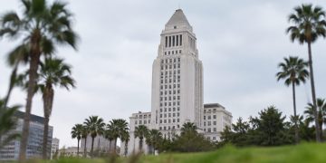 Los Angeles City Hall tower in neutral daylight, sharp above softly blurred palm trees in the foreground, illustrating the 2026 Los Angeles election.