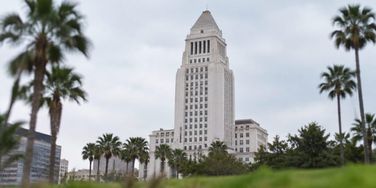 Los Angeles City Hall tower in neutral daylight, sharp above softly blurred palm trees in the foreground, illustrating the 2026 Los Angeles election.