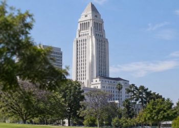 Los Angeles City Hall tower in neutral daylight, sharp above softly blurred trees, illustrating the council's public bank study vote.