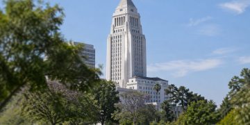 Los Angeles City Hall tower in neutral daylight, sharp above softly blurred trees, illustrating the council's public bank study vote.
