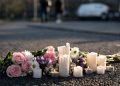 Memorial flowers and candles on blurred pavement illustrate the community's response to the student's death.
