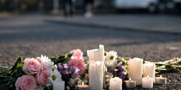 Memorial flowers and candles on blurred pavement illustrate the community's response to the student's death.