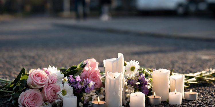 Memorial flowers and candles on blurred pavement illustrate the community's response to the student's death.