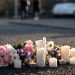 Memorial flowers and candles on blurred pavement illustrate the community's response to the student's death.