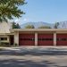 Mid-century single-story fire station with wide bay doors on a Pasadena residential street, with trees and the San Gabriel Mountains behind in daylight.