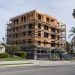 New apartment building under construction beside older single-family homes and palm trees on a Los Angeles street in neutral daylight.