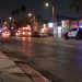 Night street scene on a wide South Los Angeles avenue, with a curb and lamp post in sharp focus and a patrol SUV blurred in the background.