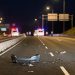 Nighttime northbound freeway lanes in Cerritos with debris on the pavement in the foreground and emergency vehicle lights blurred in the distance.