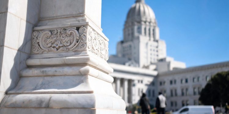 Ornamental stone column detail at Los Angeles City Hall's facade in sharp focus, with the neoclassical dome softly blurred above in midday light.