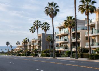 Palm-lined Ocean Avenue in Santa Monica in neutral daylight, with mid-rise beachside condominium buildings and balconies facing the Pacific.
