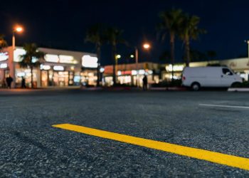 Parking lot of a commercial market in West Hollywood at night, with a yellow parking stripe in sharp focus and storefronts blurred along Santa Monica Boulevard.