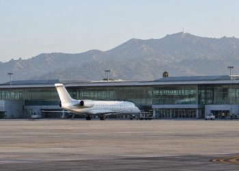 Passenger jet parked on the apron outside a modern airport terminal with a long glass facade in Burbank in soft early-morning daylight.