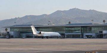 Passenger jet parked on the apron outside a modern airport terminal with a long glass facade in Burbank in soft early-morning daylight.