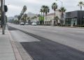 Patched asphalt and a concrete bus pad along Sunset Boulevard in West Hollywood, with palm trees and low-rise buildings in neutral daylight.