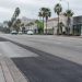 Patched asphalt and a concrete bus pad along Sunset Boulevard in West Hollywood, with palm trees and low-rise buildings in neutral daylight.