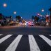 Pre-dawn Long Beach intersection with a marked crosswalk lit by street lamps in the foreground and emergency vehicles blurred far in the background.