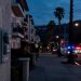 Pre-dawn residential street in Highland Park with a utility meter box in the foreground and emergency vehicles blurred in the distance.