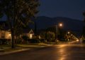 Quiet residential street of older bungalows and mature trees in Monrovia at night under street lamps, with the dark San Gabriel foothills beyond.