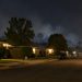 Quiet residential street of single-story homes and mature trees in West Covina at night, with a faint haze of smoke over the rooftops.