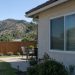 Rear of a single-story stucco house in Newbury Park with a closed kitchen window above a backyard patio and a wood fence in early-afternoon daylight.