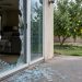 Rear of a suburban house in the San Fernando Valley with a shattered sliding glass door and glass fragments on the patio in afternoon daylight.