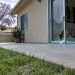 Rear patio of a single-story stucco home in Woodland Hills with a shattered sliding glass door and glass fragments on the concrete in daylight.