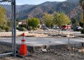 Rebuilding site in Altadena with a bare concrete foundation and temporary fencing in focus, foothills softly blurred behind, illustrating Eaton Fire recovery.