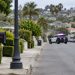 Residential street in Ladera Heights in daylight, with a mailbox and lamp post in the foreground and a patrol SUV blurred in the background.