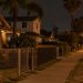 Residential street in Westmont at night with stucco homes, palm trees and an empty sidewalk under street lamps, seen from a long-lens view.