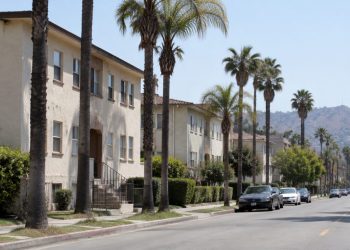 Residential street of older stucco apartment buildings and palm trees on the Westside of Los Angeles in afternoon daylight, seen through a long lens.