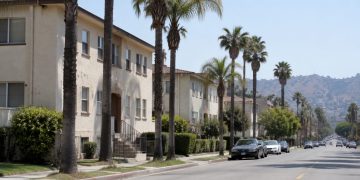 Residential street of older stucco apartment buildings and palm trees on the Westside of Los Angeles in afternoon daylight, seen through a long lens.
