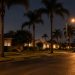 Residential street of single-story stucco homes and palm trees in Santa Ana at night, lit by street lamps, with a front lawn in the foreground.