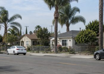 Residential street of single-story stucco homes, front yards and palm trees in Santa Ana, photographed from across the street in neutral daylight.