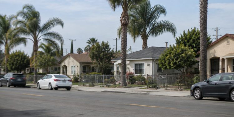 Residential street of single-story stucco homes, front yards and palm trees in Santa Ana, photographed from across the street in neutral daylight.