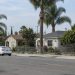 Residential street of single-story stucco homes, front yards and palm trees in Santa Ana, photographed from across the street in neutral daylight.