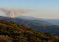 Rugged Santa Monica Mountains ridgelines covered in chaparral with a gray smoke plume rising from a distant ridge in late-afternoon daylight.