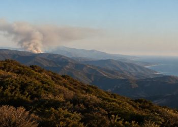 Rugged Santa Monica Mountains ridgelines covered in chaparral with a gray smoke plume rising from a distant ridge in late-afternoon daylight.