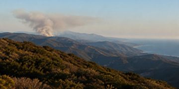 Rugged Santa Monica Mountains ridgelines covered in chaparral with a gray smoke plume rising from a distant ridge in late-afternoon daylight.