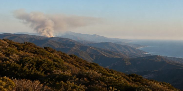 Rugged Santa Monica Mountains ridgelines covered in chaparral with a gray smoke plume rising from a distant ridge in late-afternoon daylight.