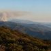 Rugged Santa Monica Mountains ridgelines covered in chaparral with a gray smoke plume rising from a distant ridge in late-afternoon daylight.