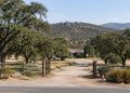 Rural Valley Center property with a dirt driveway, live oaks and dry chaparral hills in neutral daylight, illustrating a San Diego County murder case.