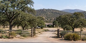 Rural Valley Center property with a dirt driveway, live oaks and dry chaparral hills in neutral daylight, illustrating a San Diego County murder case.